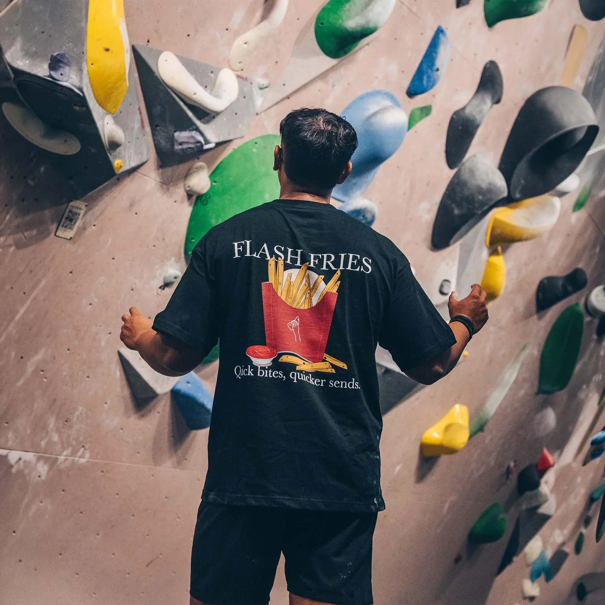 Climber facing a colourful bouldering wall with arms outstretched, reading the route