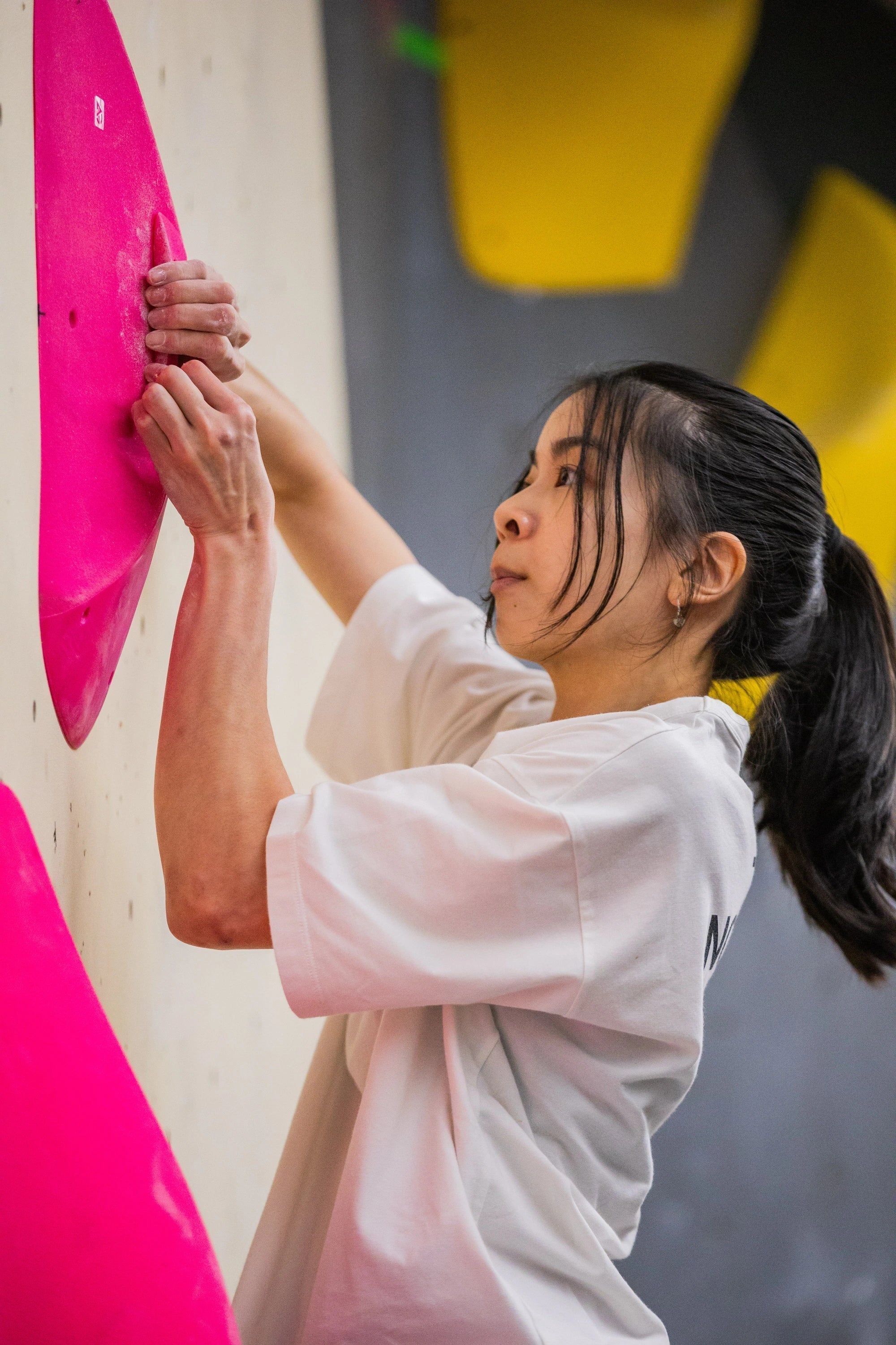 Female climber reaching up to grip a large pink sloper on an indoor bouldering wall