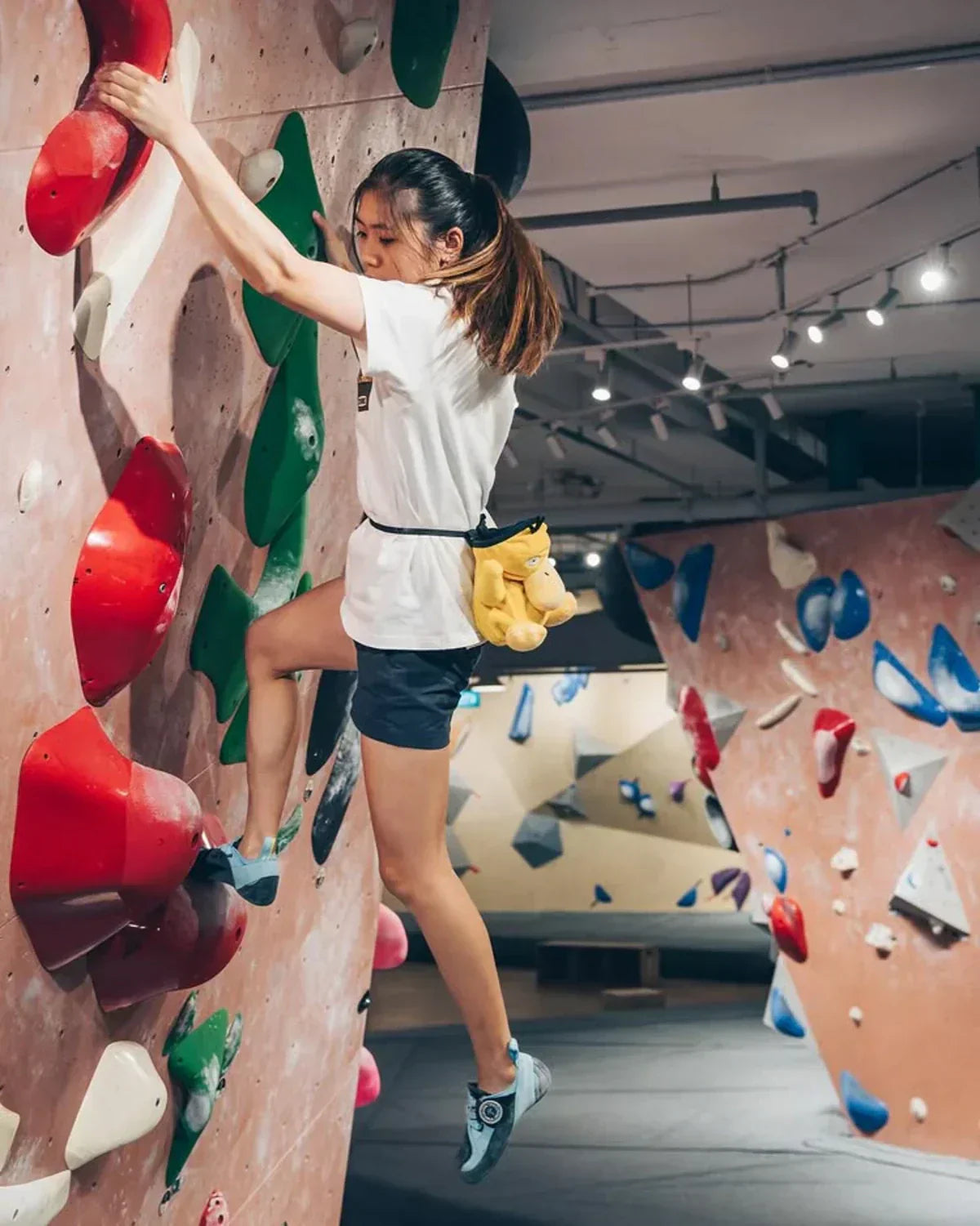 Climber high up on a boulder wall indoors with colorful holds.