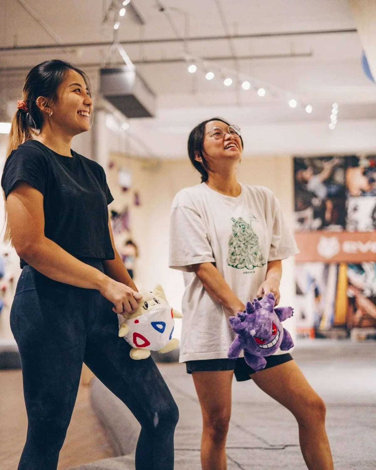 Two female climbers smiling and facing bouldering wall in climbing gym