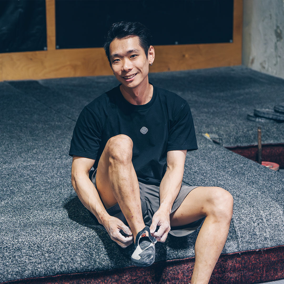 Male climber on bouldering mat removing shoes to take a rest between attempts