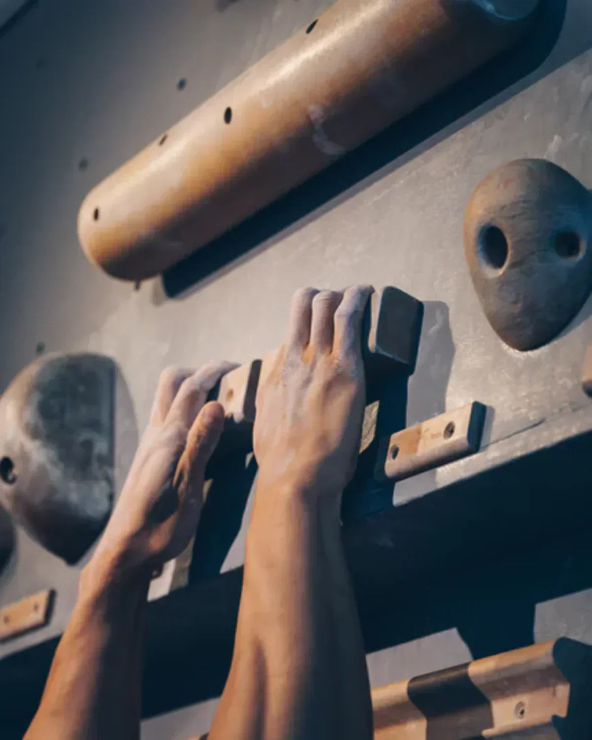 Close-up of chalked hands gripping holds on an indoor climbing woody board