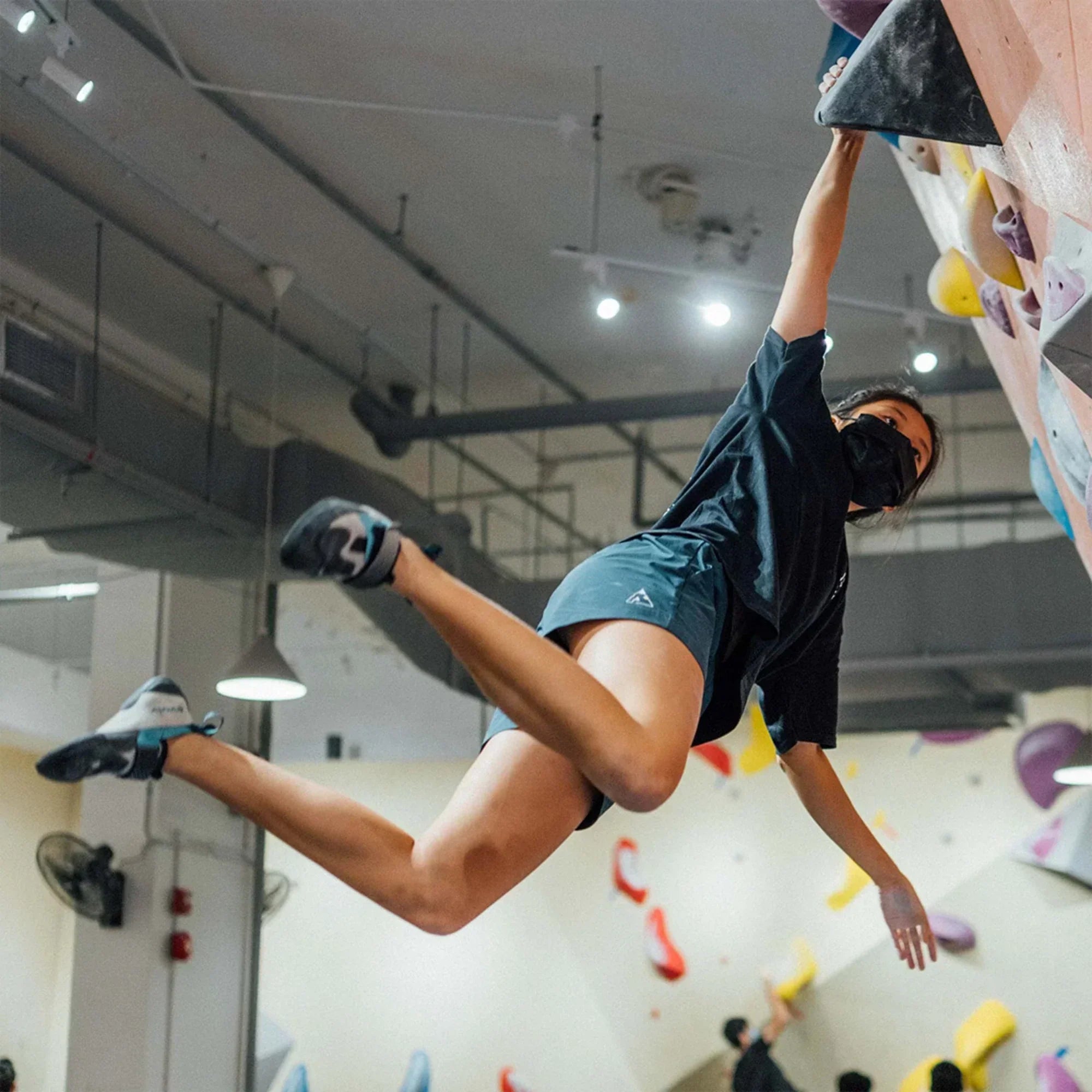 Female climber making a dynamic move and hanging off one arm on an indoor bouldering wall