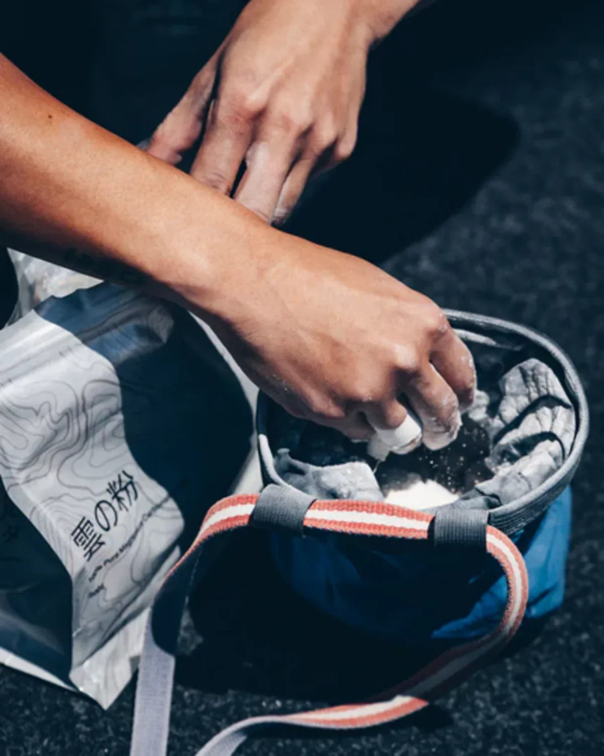 Climber refilling a chalk bag from a Kumo powder chalk bag on a bouldering mat